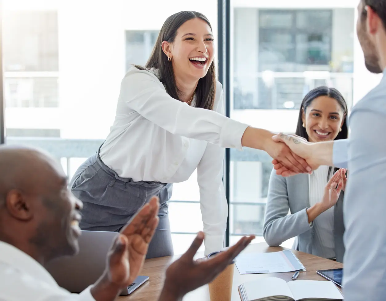 A woman shaking hands with another person in front of other people.