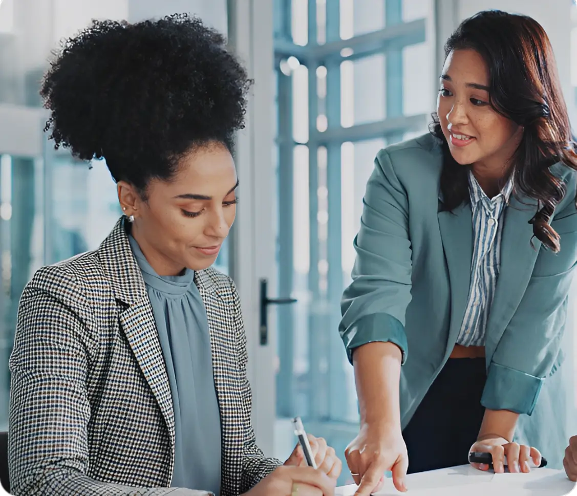 Two women in a room with papers and pens.